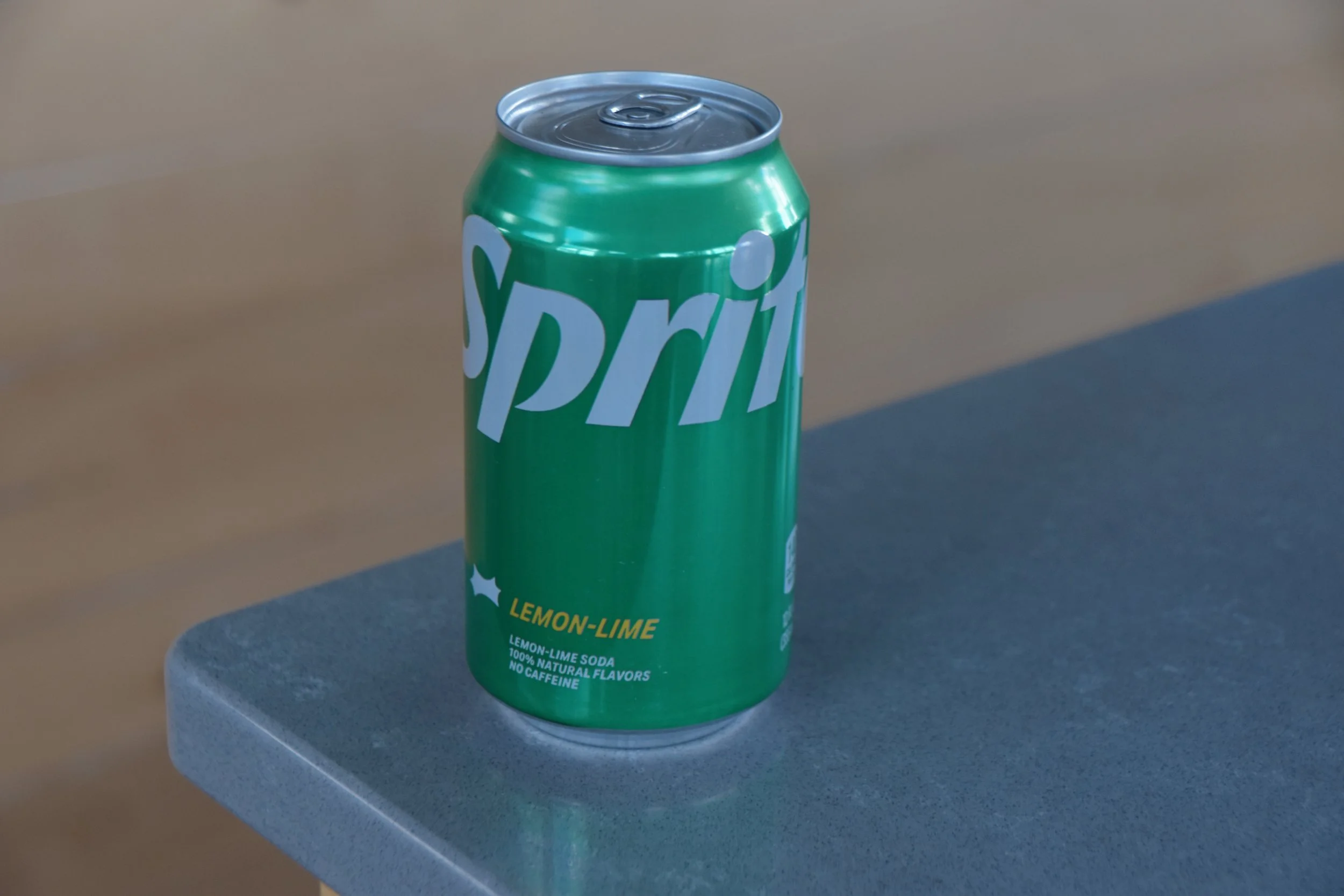 A green can of Sprite Lemon-Lime soda placed on a gray surface, with a plain background.