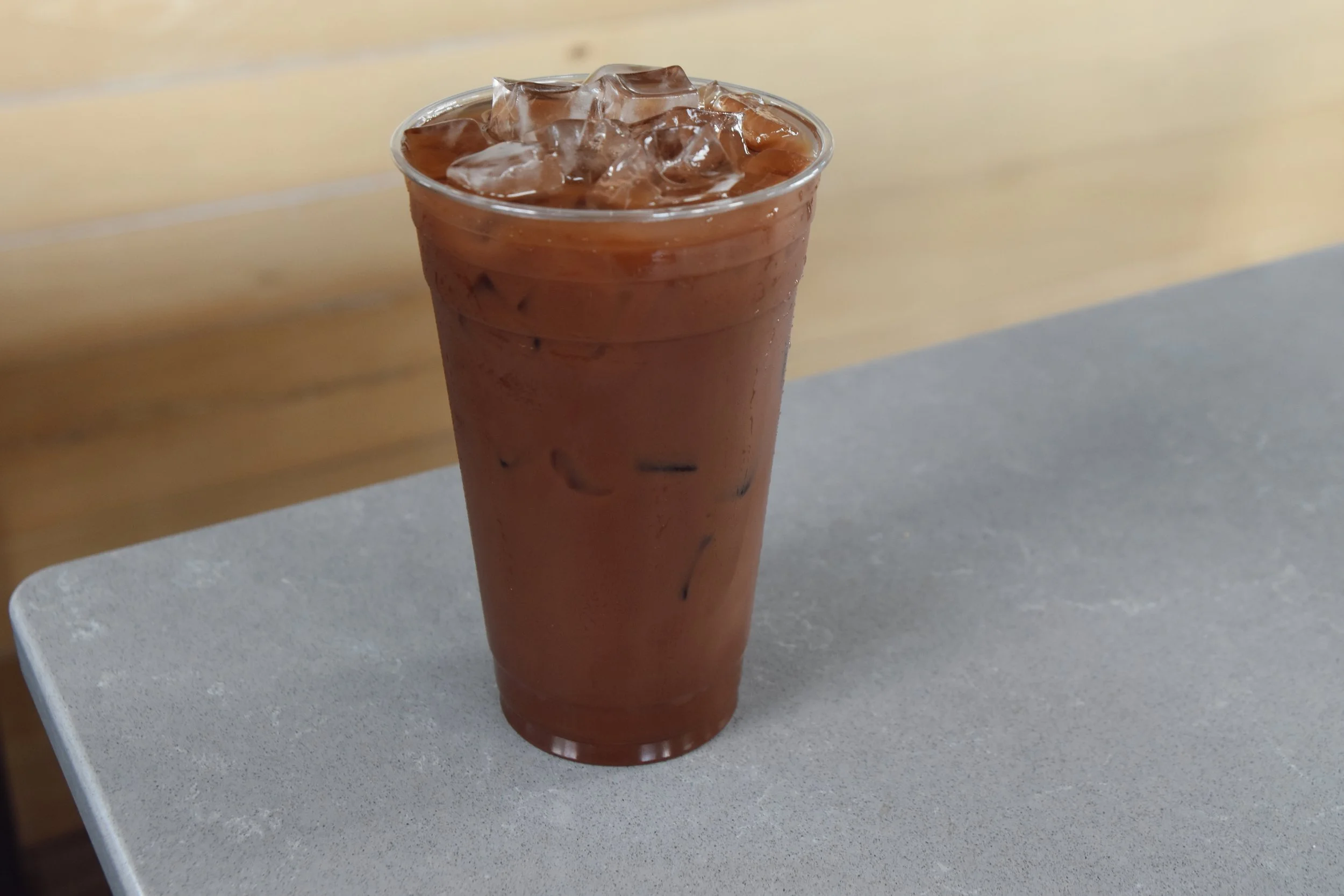 A tall glass of iced chocolate drink with ice cubes, placed on a gray table with a blurred background.
