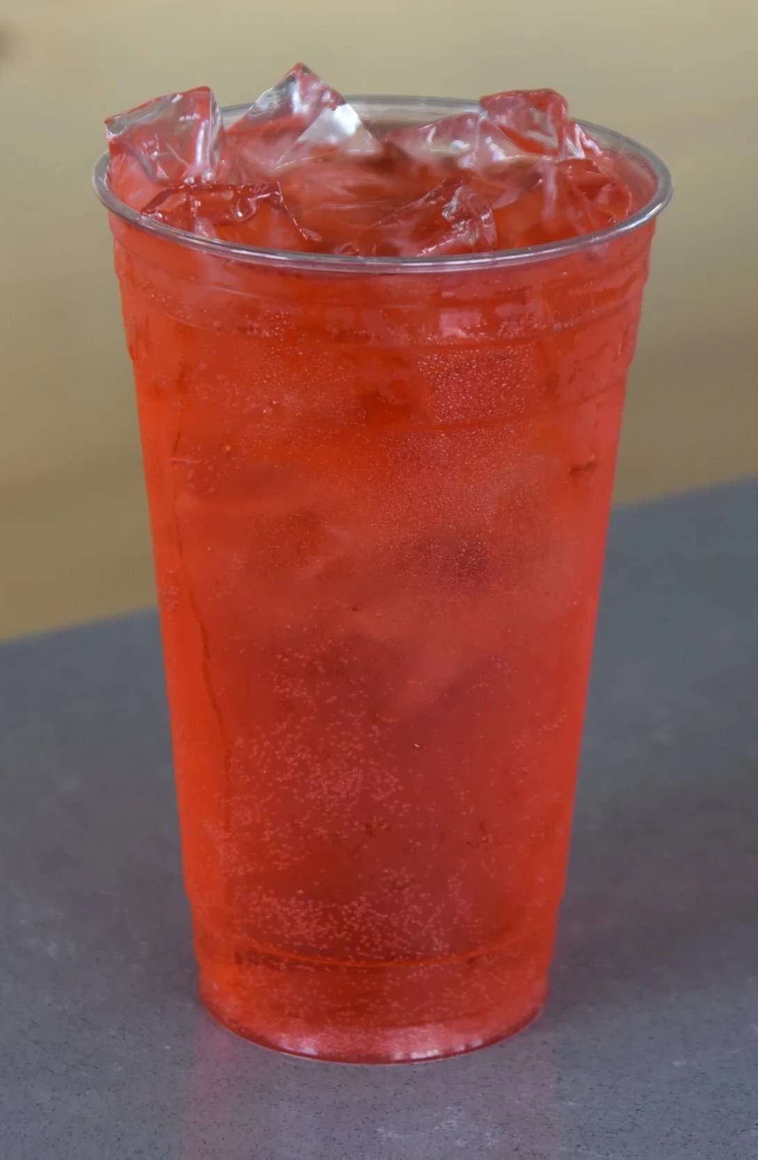 A tall transparent glass filled with orange-colored iced beverage and ice cubes.