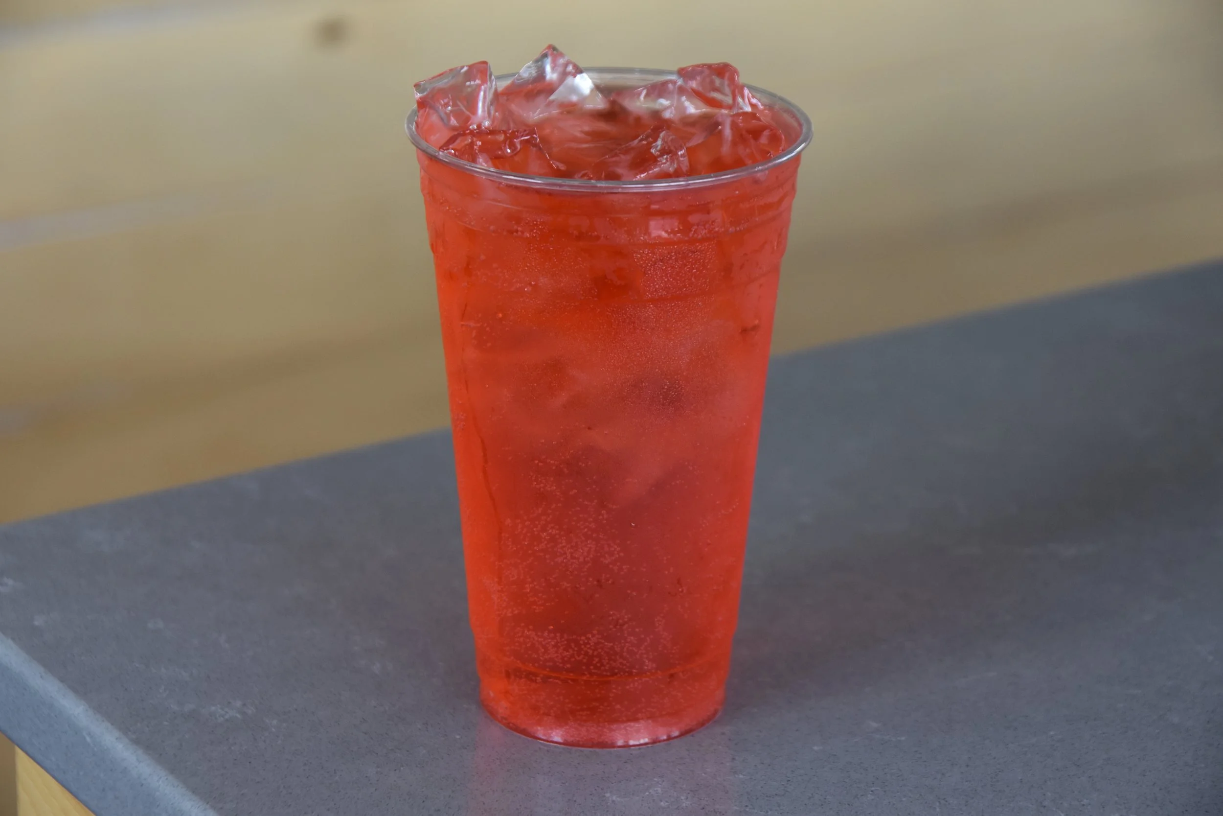 A clear plastic cup filled with orange-colored beverage and ice cubes.