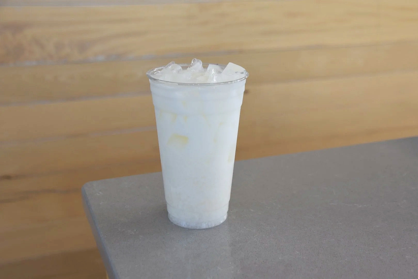 Glass of iced milk with ice cubes on a grey surface with a wooden background.