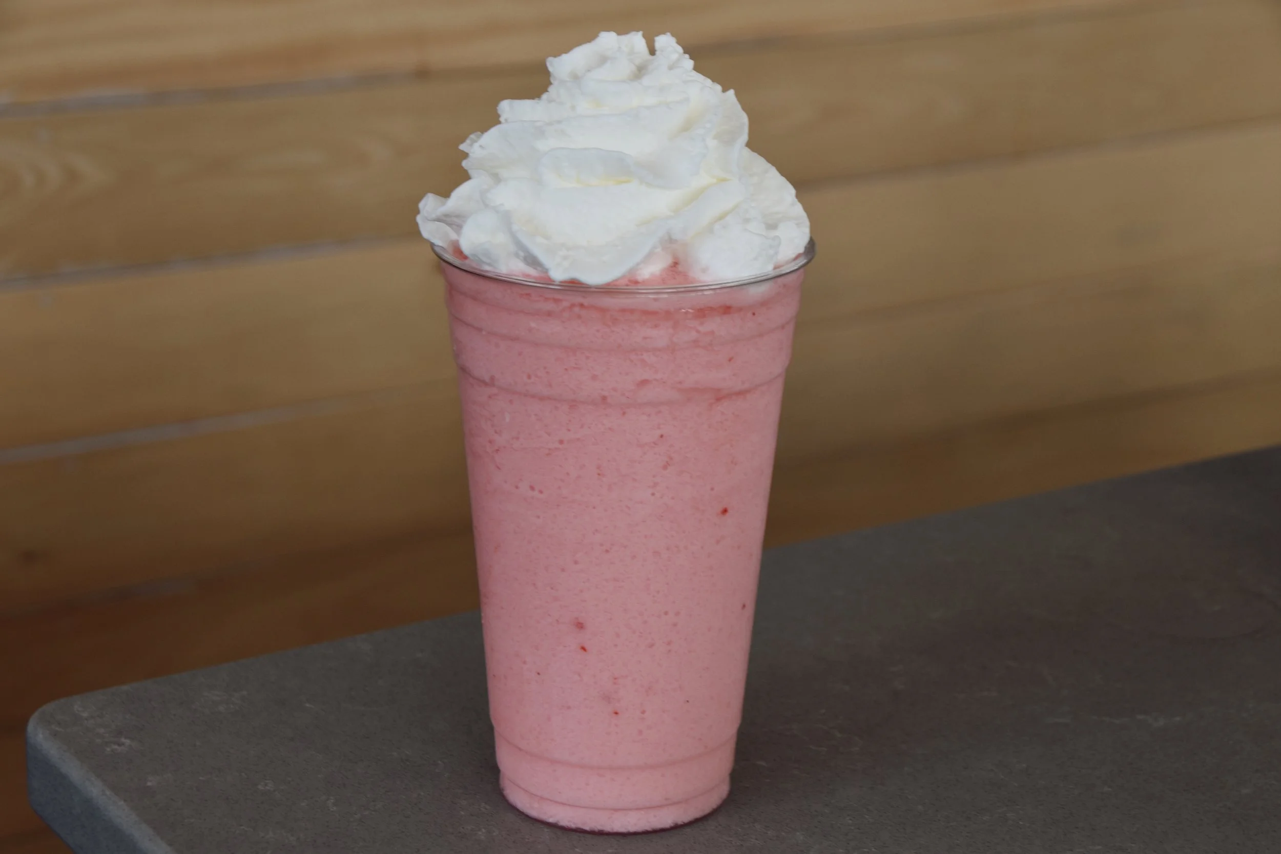 A pink strawberry milkshake topped with whipped cream in a clear glass