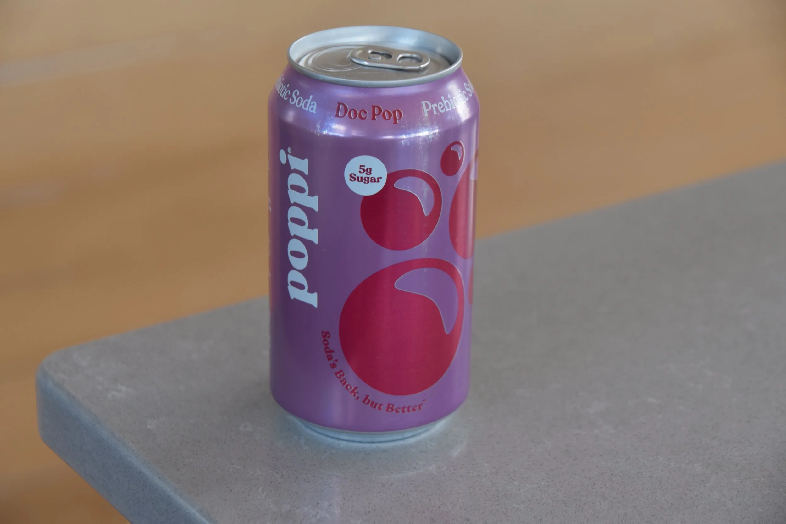 A purple soda can labeled 'Pop' with a red cherry graphic, placed on a gray rock surface.