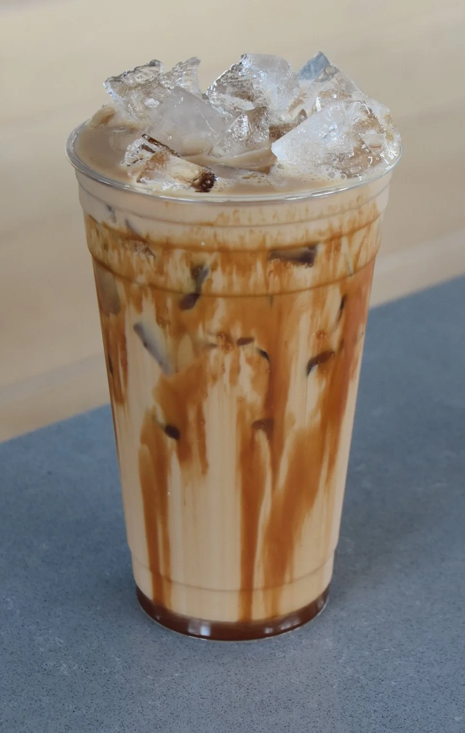 Iced coffee with milk, chocolate syrup, and ice cubes in a clear plastic cup.