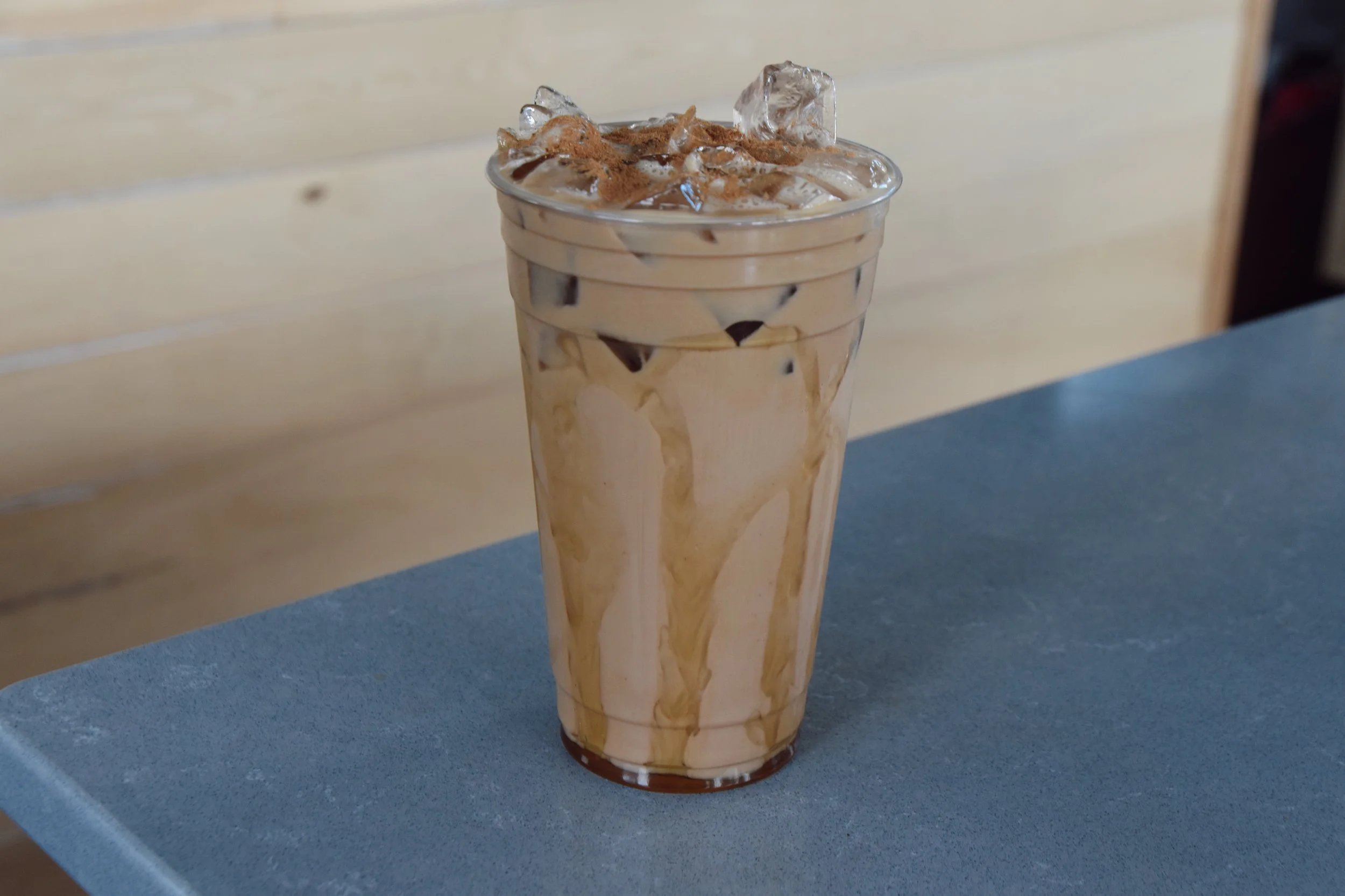 A tall glass of iced coffee topped with ice cubes, whipped cream, and sprinkled with cocoa powder