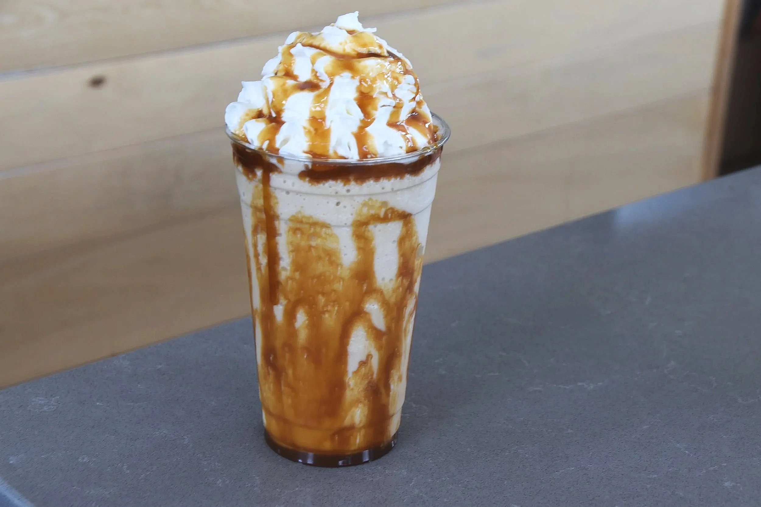 A tall glass of vanilla milkshake topped with whipped cream and caramel drizzle, with caramel syrup running down the sides of the glass.