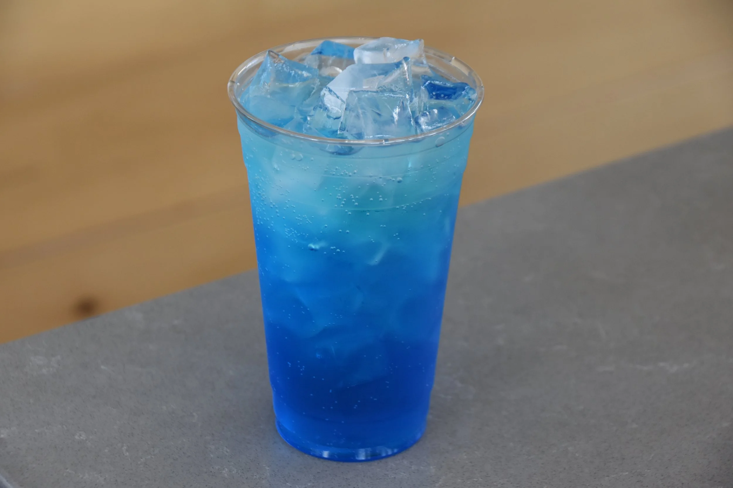 A clear plastic cup filled with blue carbonated soda and ice cubes.