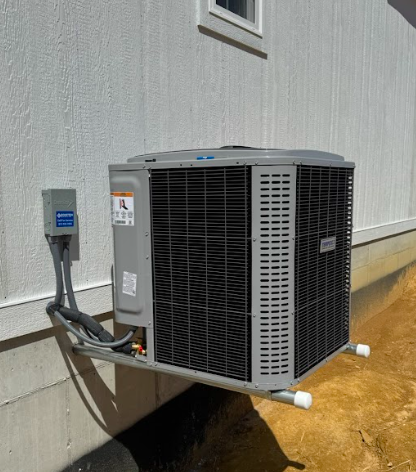 An outdoor air conditioning unit mounted on the side of a building with electrical connections and vent pipes.
