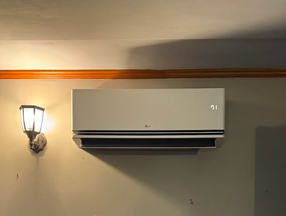 Wall-mounted LG air conditioner with digital display showing 71°F, adjacent to a wall-mounted lamp with a decorative shade.