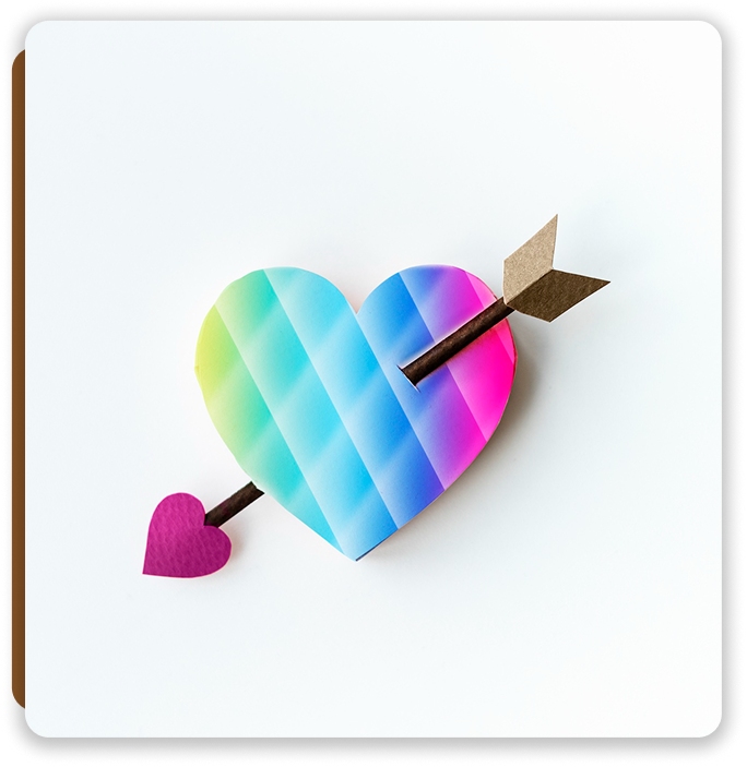 Heart-shaped rainbow-colored paper with an arrow piercing through it, placed on a white background.
