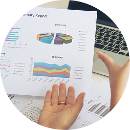 Person holding financial report with colorful charts and graphs, a laptop in the background, and another document on the table.