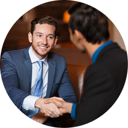 Two men in business suits shaking hands and smiling in a professional setting.