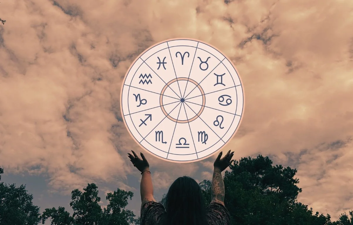 A person with long hair and tattoos on their arms standing outdoors at dusk with their arms raised towards the sky, reaching for a large circle of zodiac signs floating in the sky surrounded by clouds.