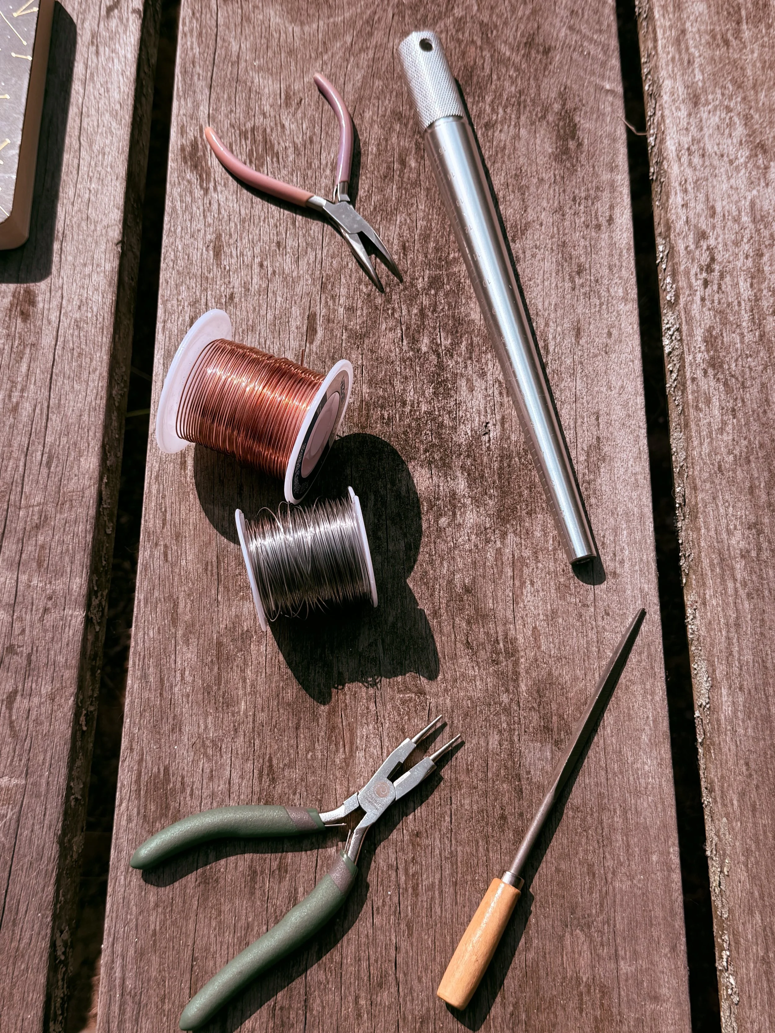 Tools on a wooden surface, including copper wire spool, clip pliers, long needle-nose pliers, and a wooden handled awl.