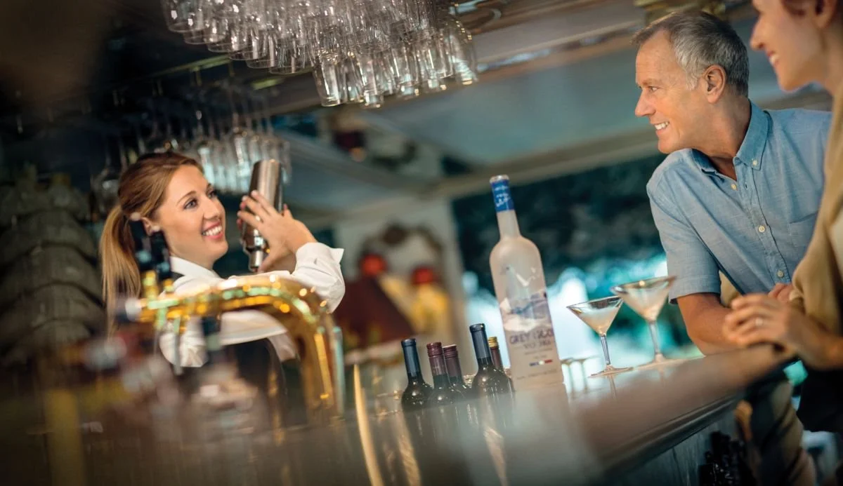A bartender serving drinks at a bar with two customers, a man and a woman, engaging in conversation.
