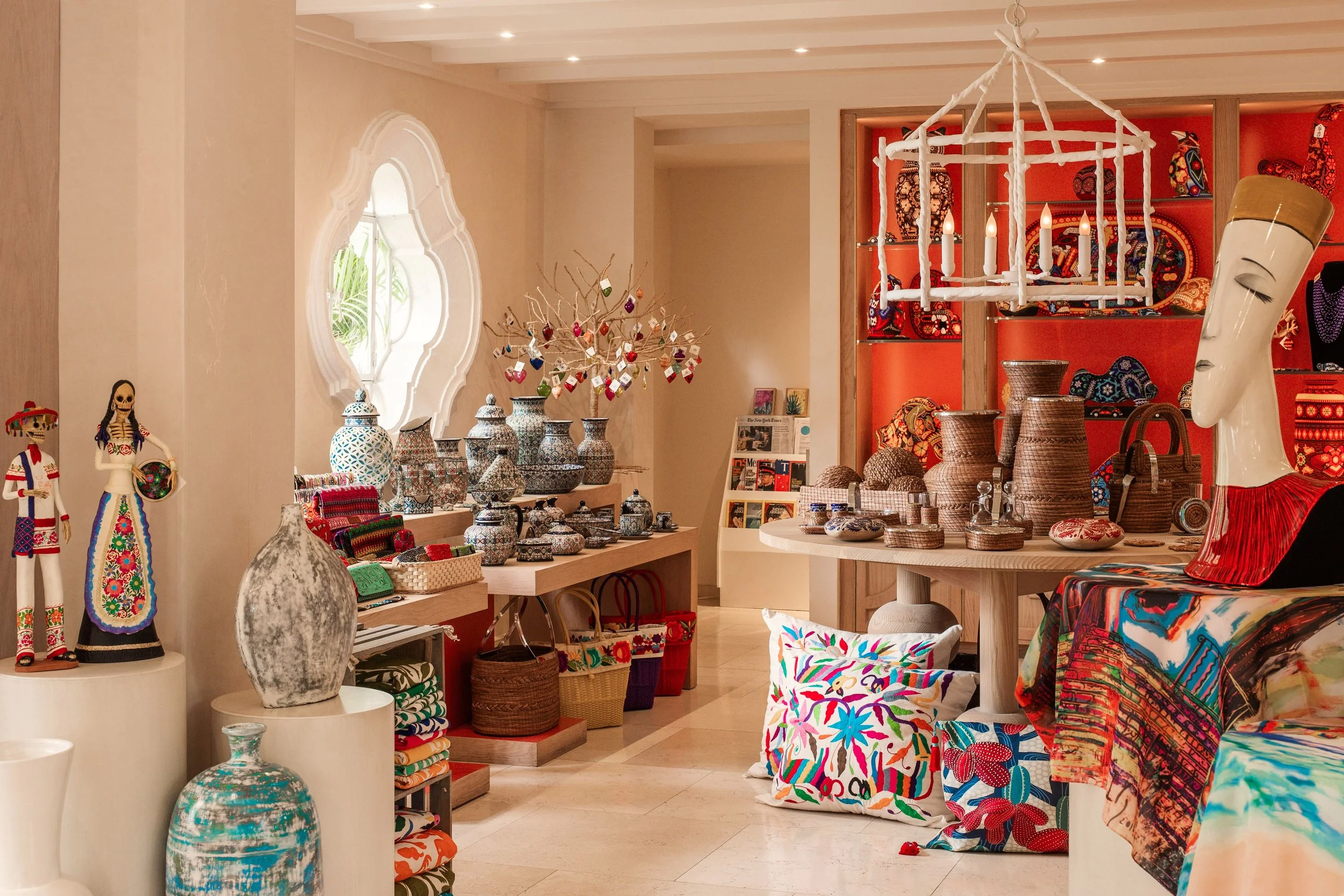 Inside a store displaying colorful decorative items, vases, textiles, and accessories, with a woven chandelier hanging from the ceiling.