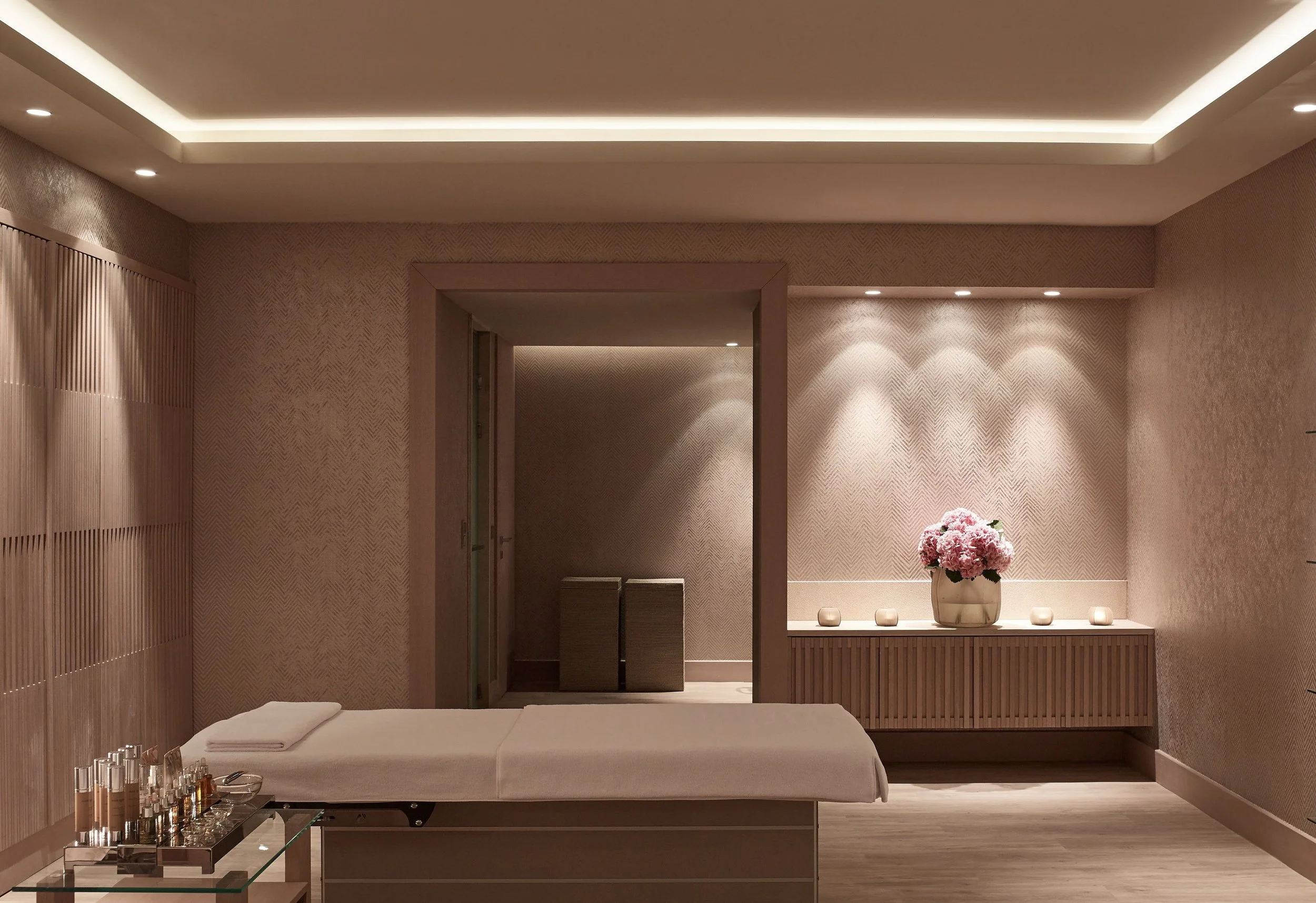 A spa or massage room with a bed, towels, a flower arrangement, and soft lighting.