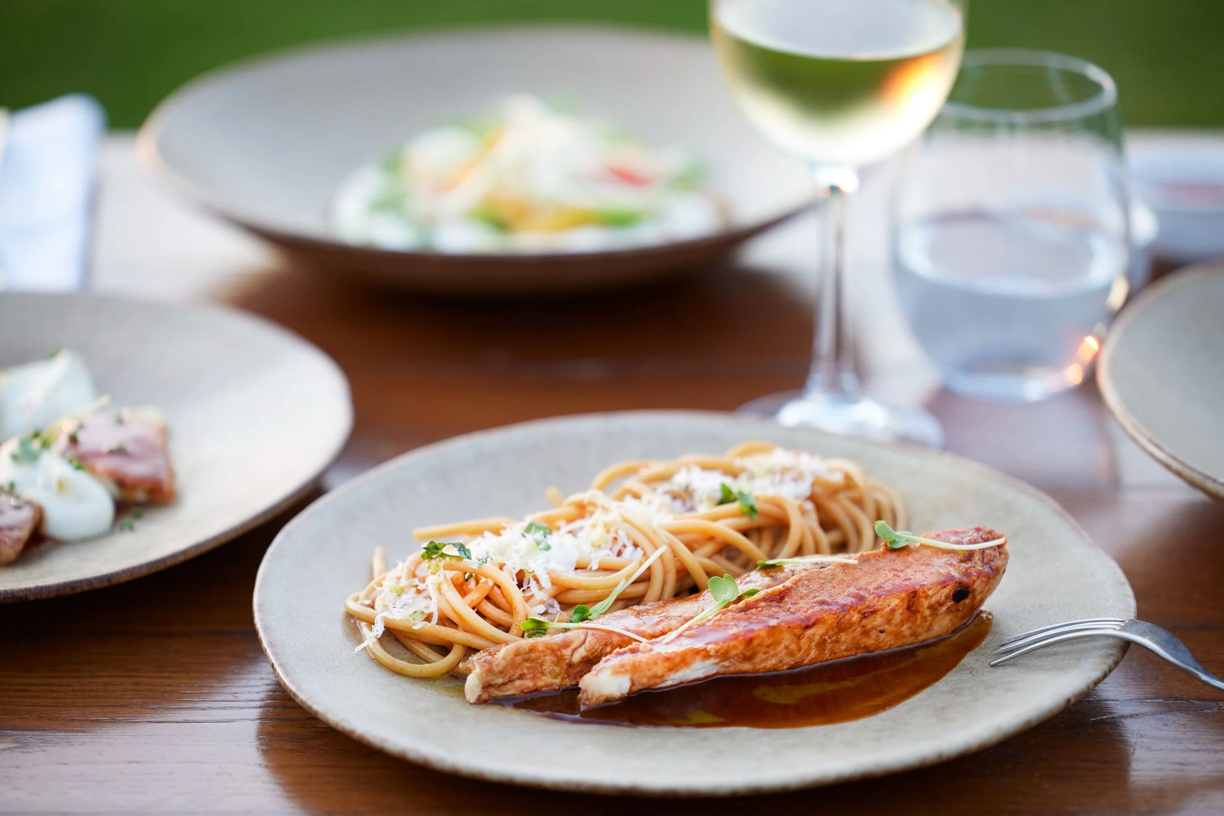 Plate of spaghetti with tomato sauce topped with grated cheese and garnished with microgreens, served with a grilled chicken breast, on a ceramic plate, with a glass of white wine in the background.