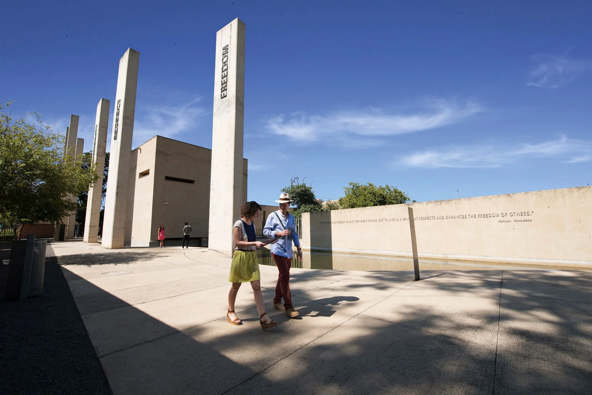 People walking and talking at the Martin Luther King Jr Memorial in Washington, D.C., with tall white stone pillars and a blue sky.