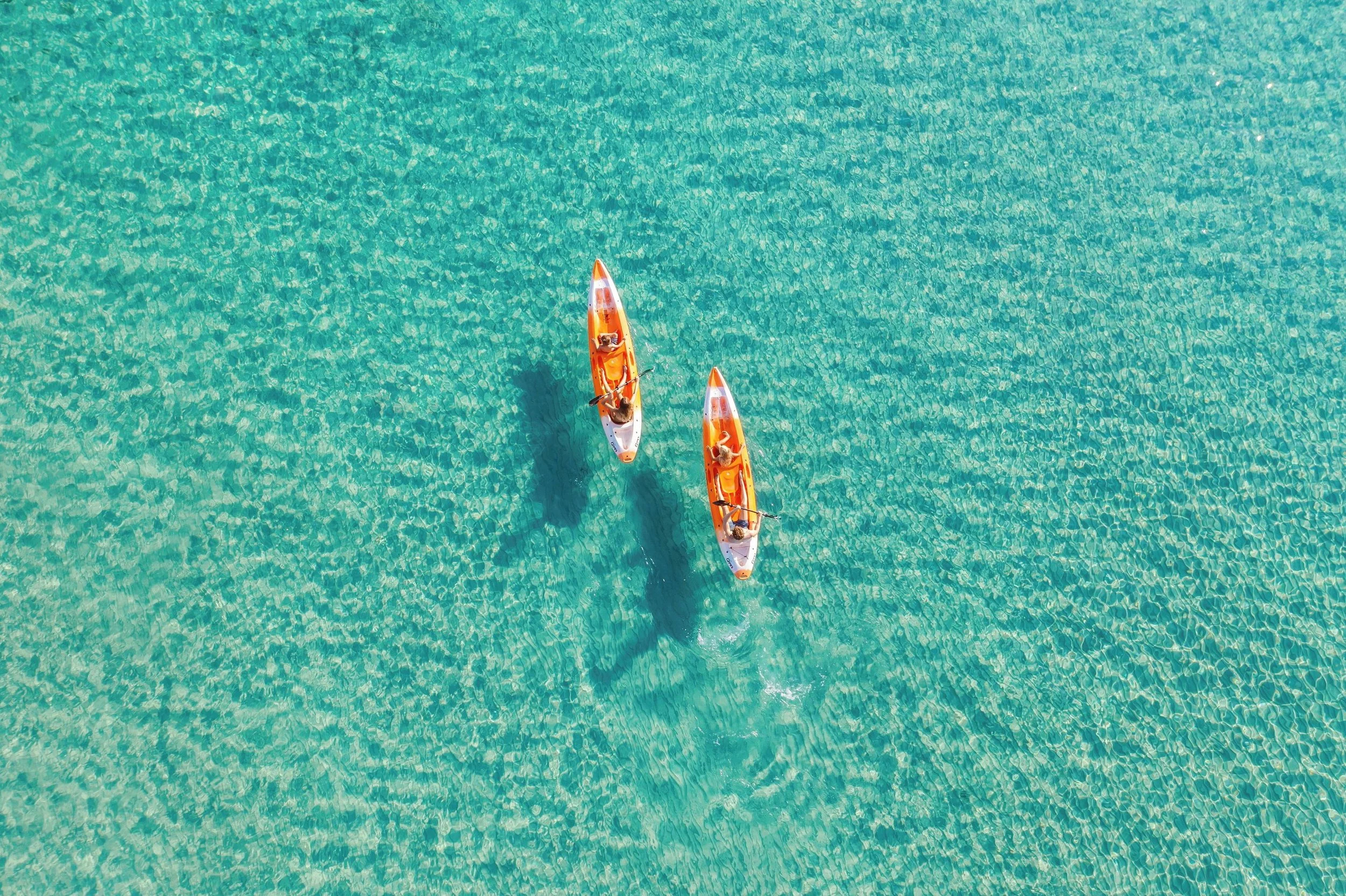 Two people kayaking in clear turquoise water with a top-down view.
