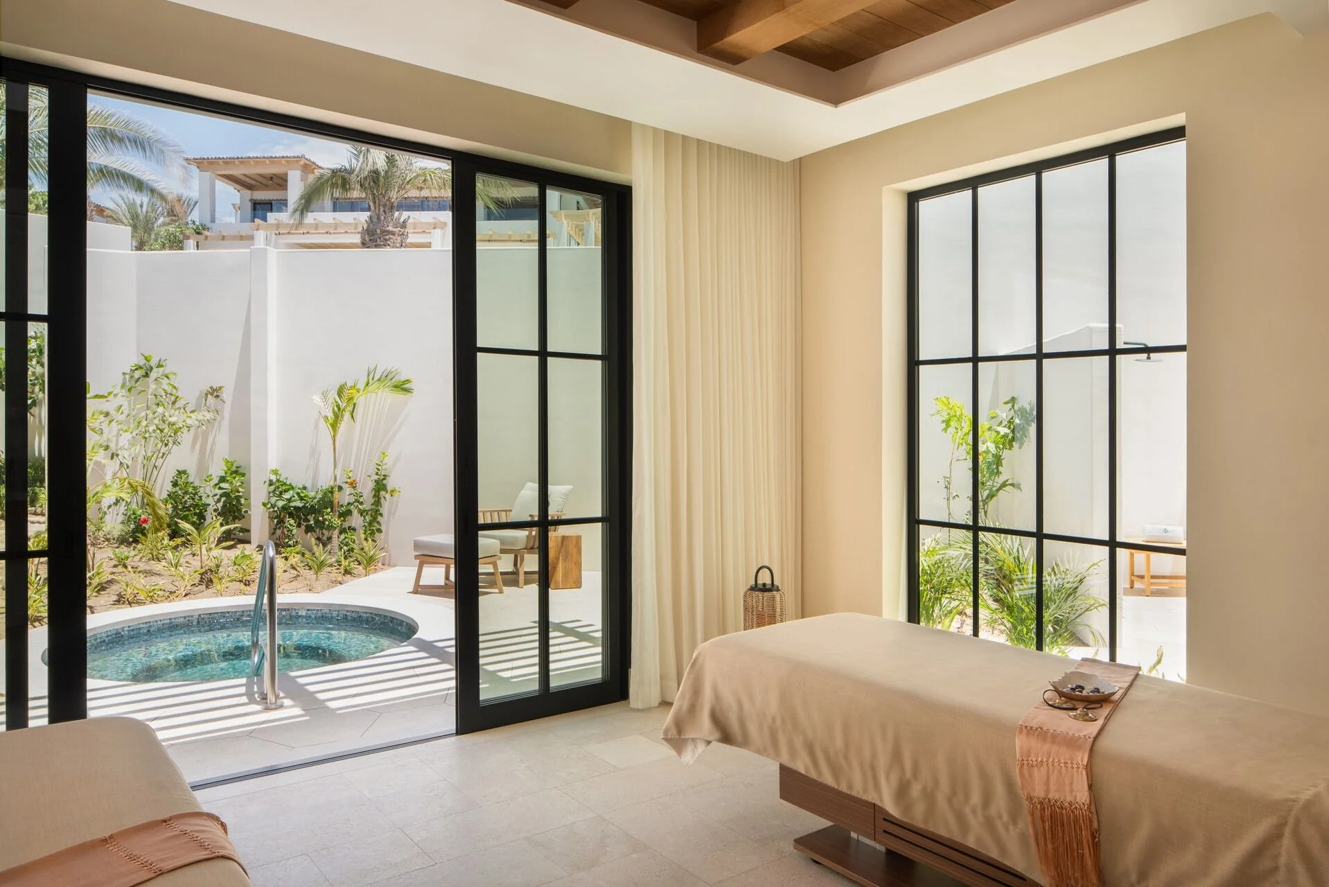 Interior of a room with large glass sliding doors opening to a patio with a small pool, lounge chair, and potted plants, in a sunny outdoor setting.