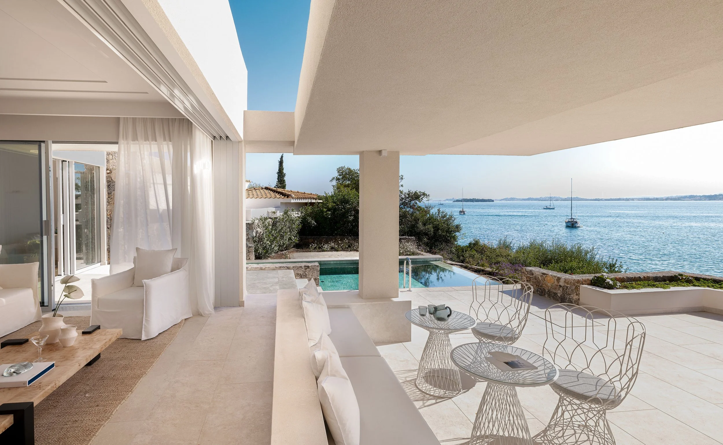 Modern outdoor patio with white furniture, a view of a body of water with sailboats, and a blue sky.