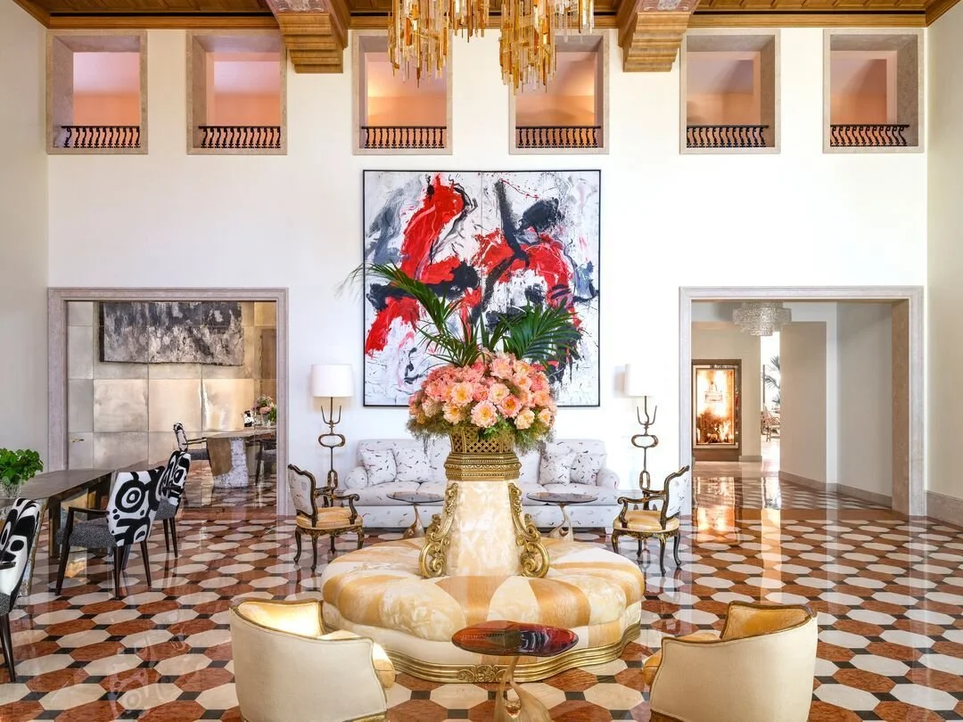 Elegant hotel lobby with a large floral arrangement centerpiece on a round table, a white sofa, and colorful abstract artwork on a high white wall, with a checkerboard-patterned marble floor and modern decor.