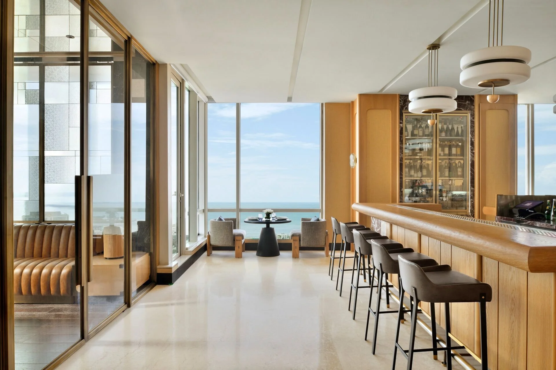 Luxury hotel bar with barstools, a marble counter, and an ocean view through large windows.