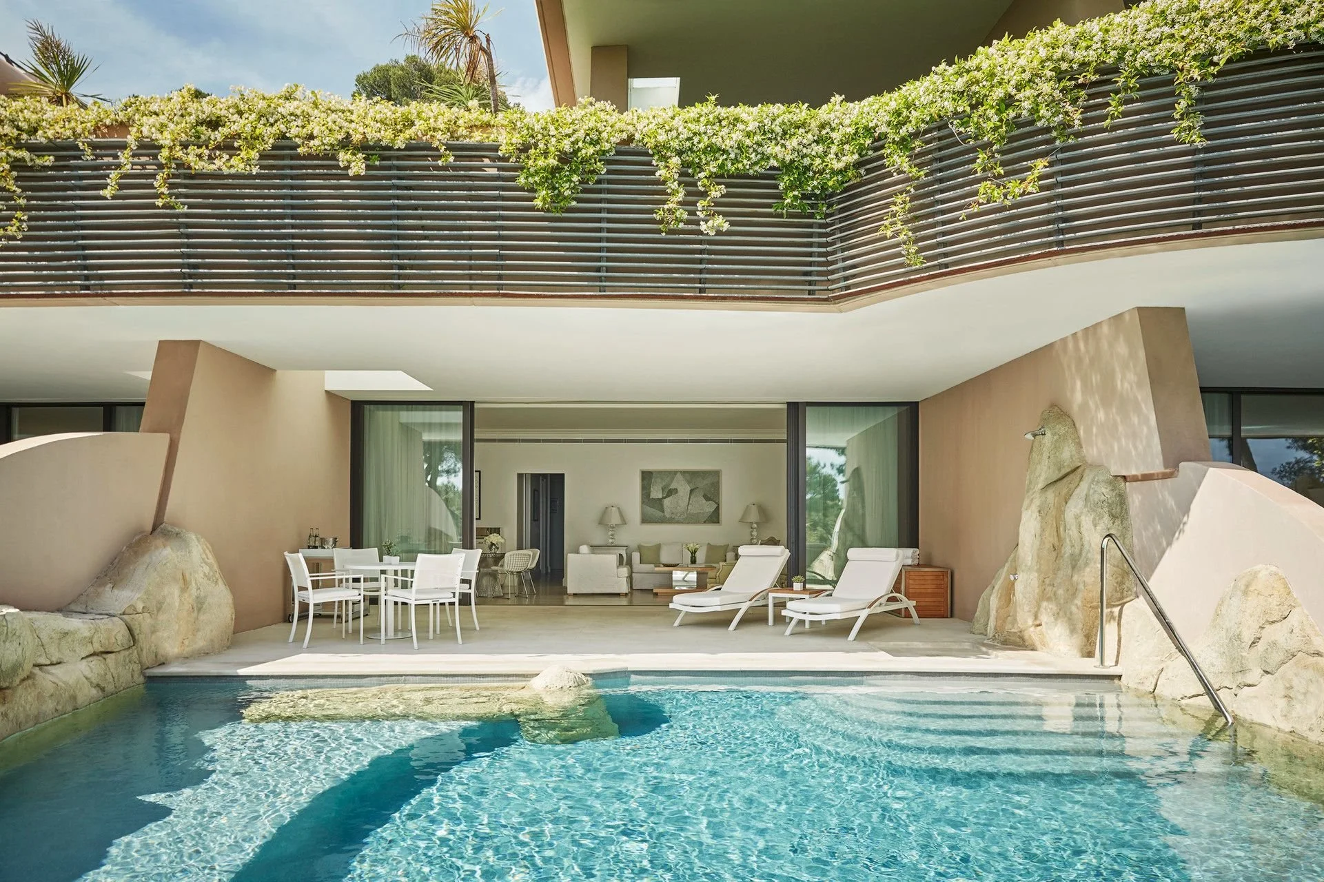 Modern house with balcony covered in greenery, outdoor seating and pool with rocks.