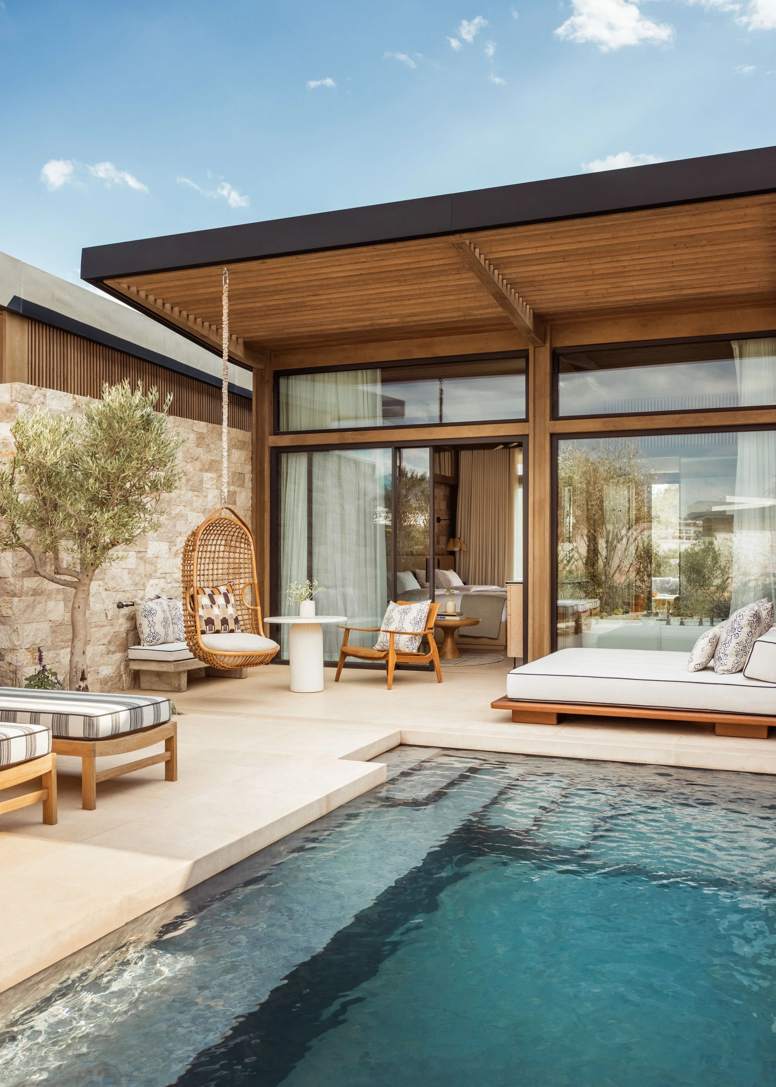 Modern house with large glass windows, outdoor seating area, and swimming pool in the backyard, under a clear blue sky.