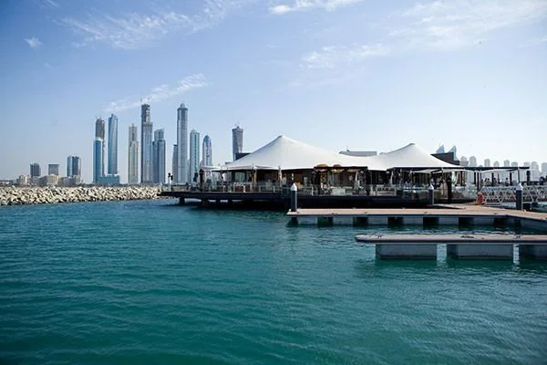  waterfront with a city skyline featuring skyscrapers in the background, a pier with a large white tent, and calm blue water in the foreground