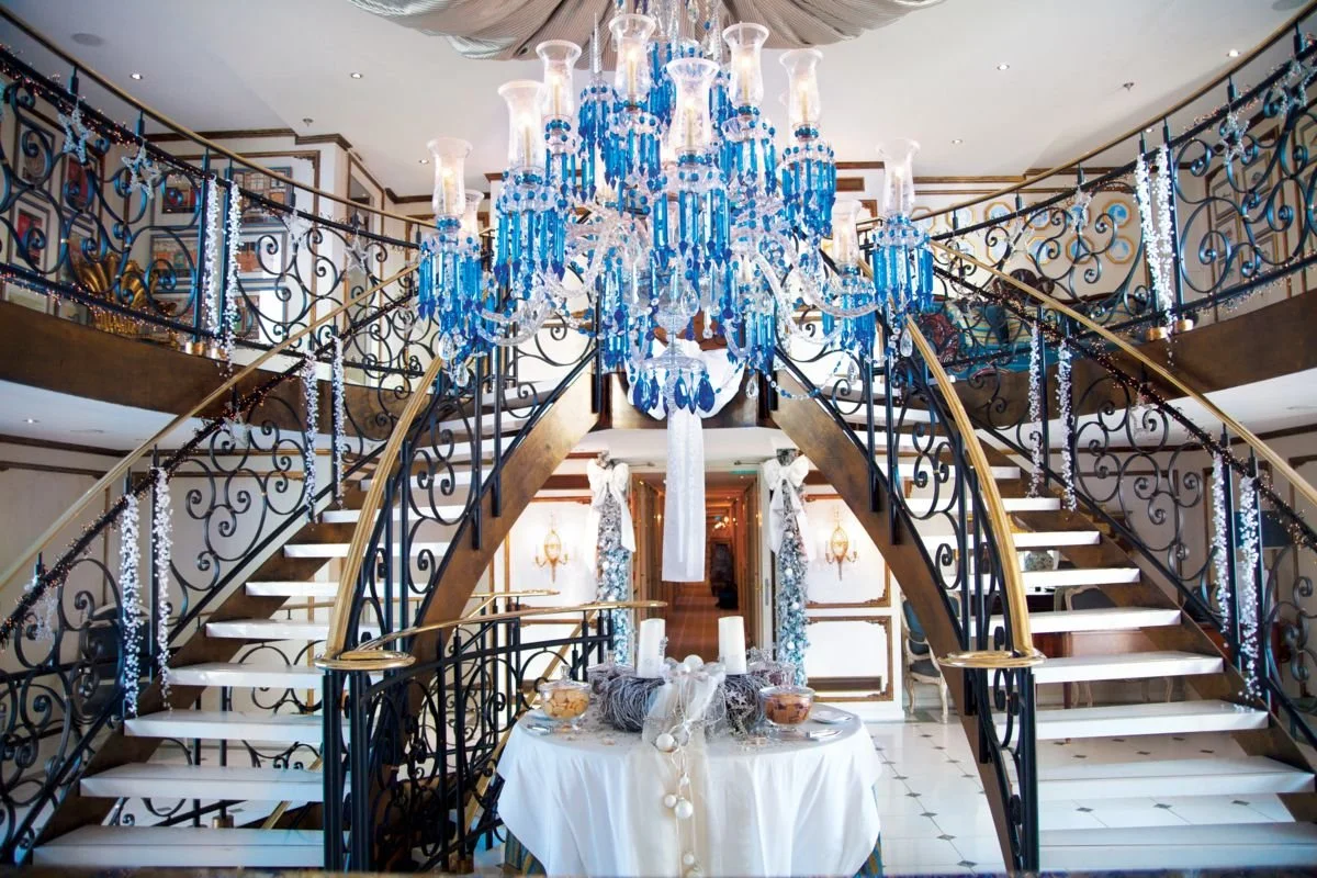 Interior of an elegant building with a grand staircase, a large blue and white chandelier, and decorated with white and blue accents for a festive celebration.