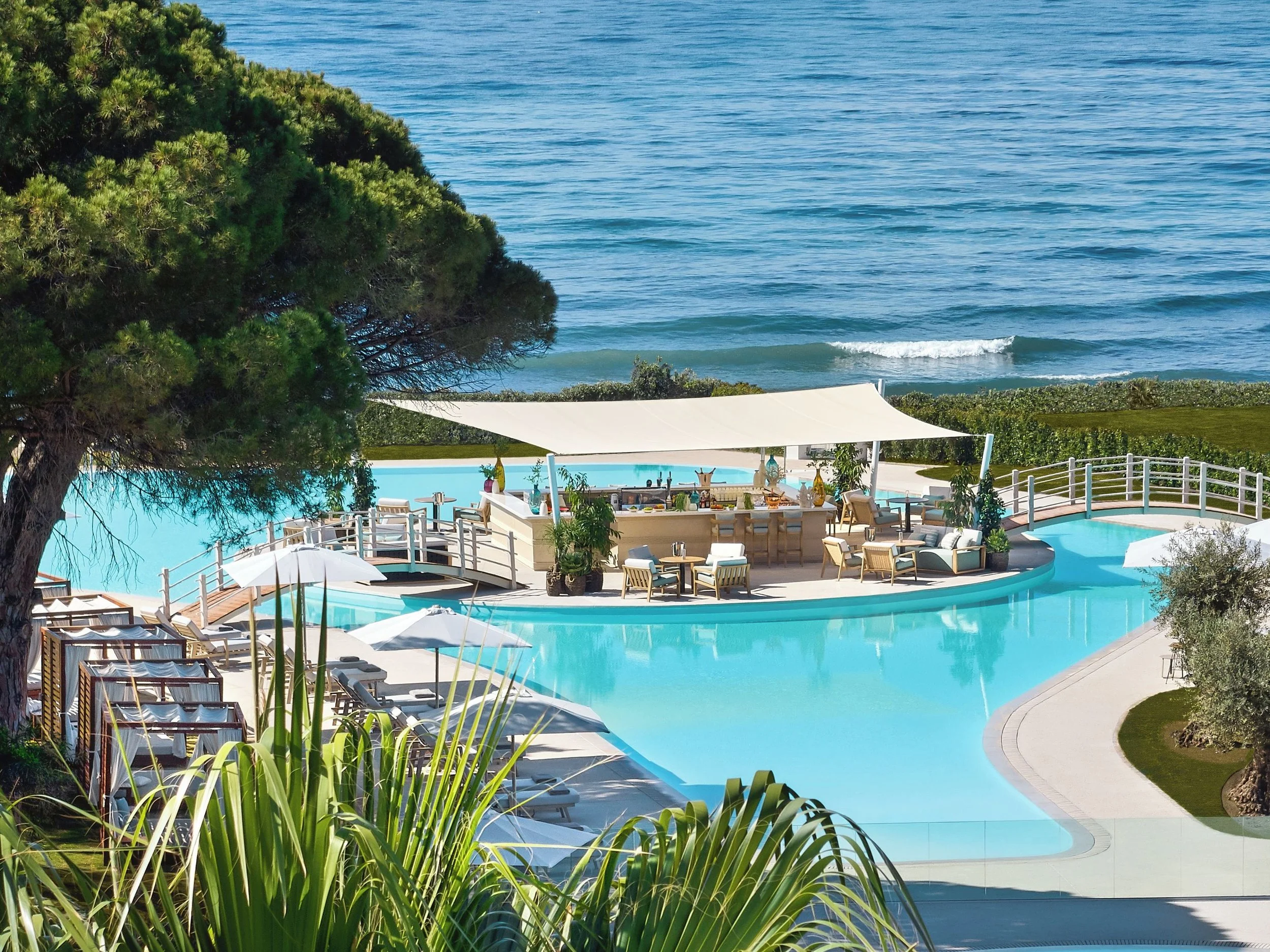 Resort pool area overlooking the ocean with lounge chairs, umbrellas, and lush greenery.