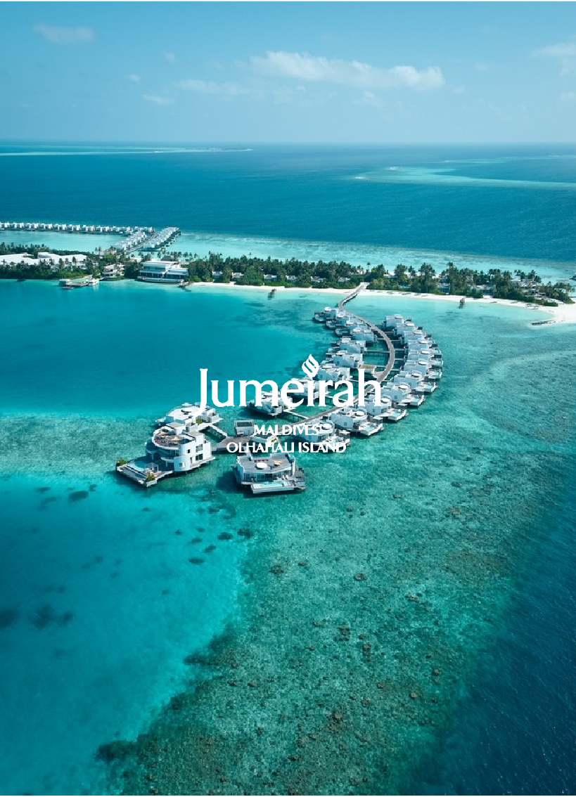 Aerial view of a luxury overwater bungalow resort in the Maldives, with turquoise waters, white sandy beaches, and a nearby island with lush greenery.