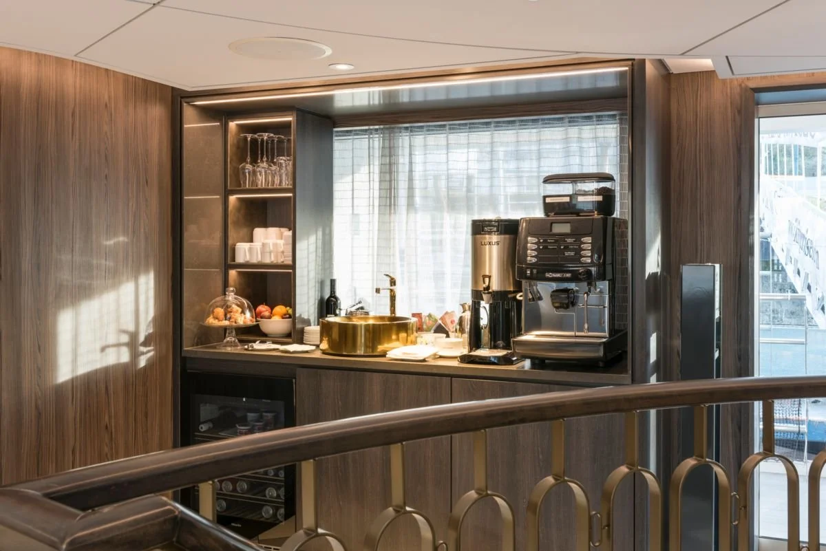 Coffee and beverage station in a modern room with wood-paneled walls, a window, and various brewing equipment.