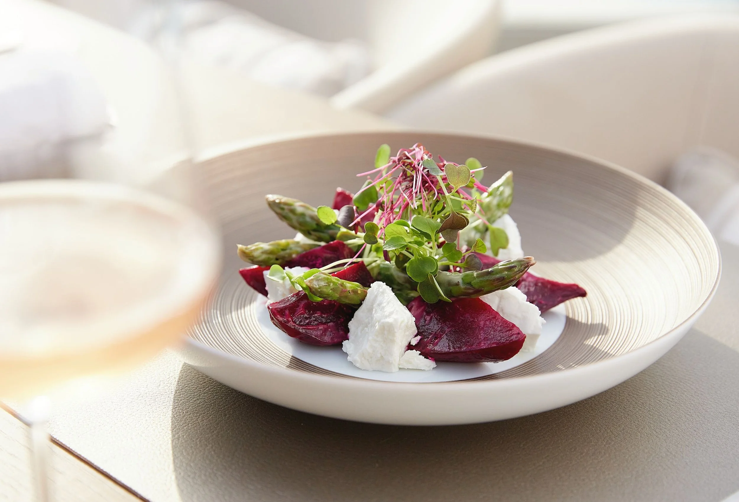 A plate of salad containing roasted beets, asparagus, fresh greens, and dollops of white cheese or cream, garnished with microgreens, on a white plate.