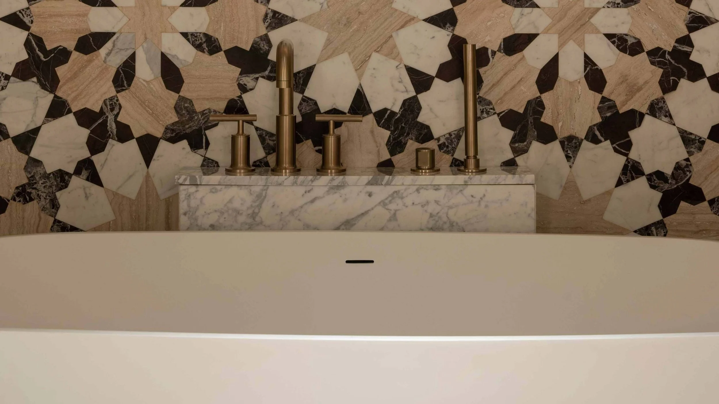 Close-up of bathroom sink fixtures with a marble countertop and geometric patterned tile wall in the background.