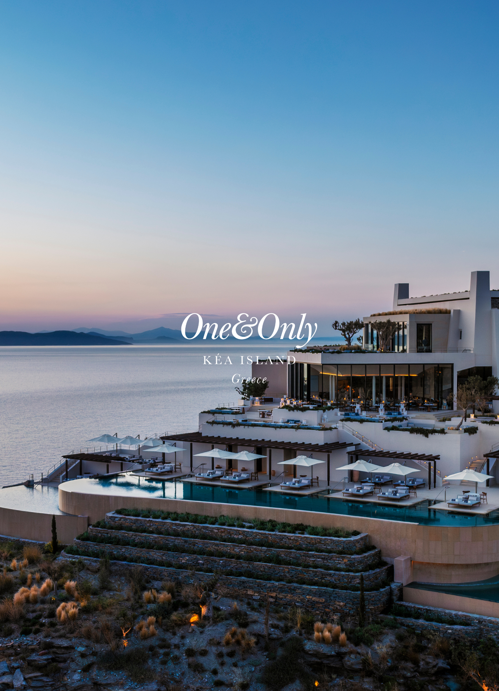 Luxury hotel or resort with infinity pool on a hillside overlooking the ocean at sunset, with modern white buildings and umbrellas on terrace, in Greece.
