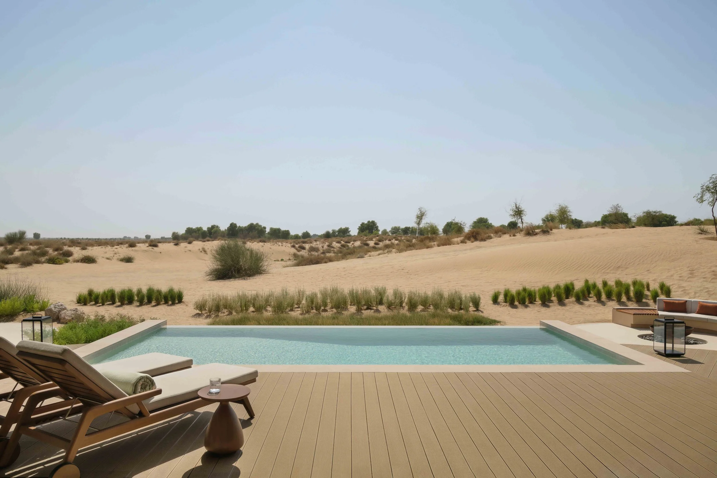 Desert landscape seen from a backyard patio with pool, lounge chairs, and decorative lanterns.