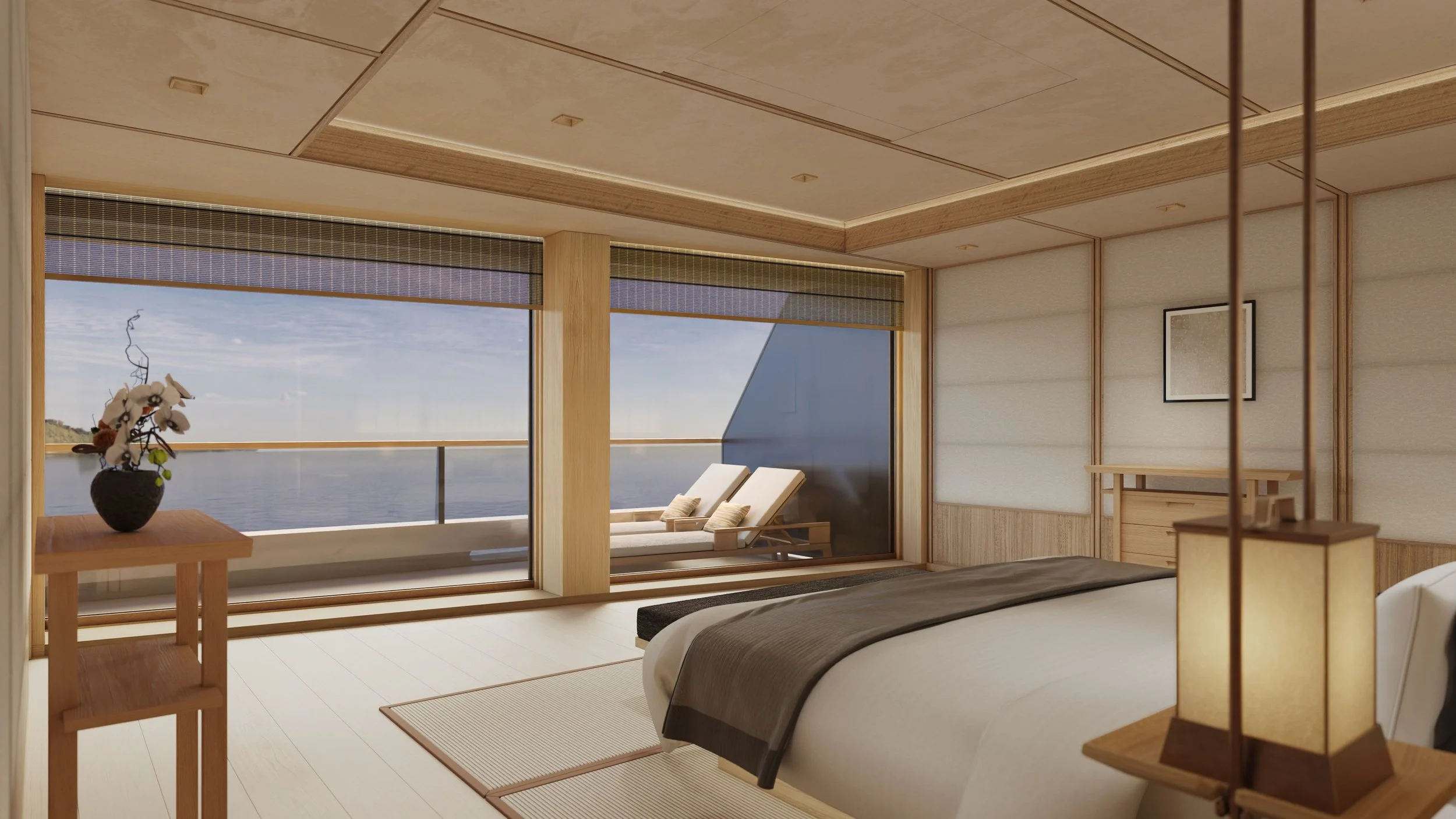 A minimalist hotel room with large windows overlooking water, featuring a bed with gray linens, a wooden side table with a flower arrangement, and two lounge chairs on a balcony.