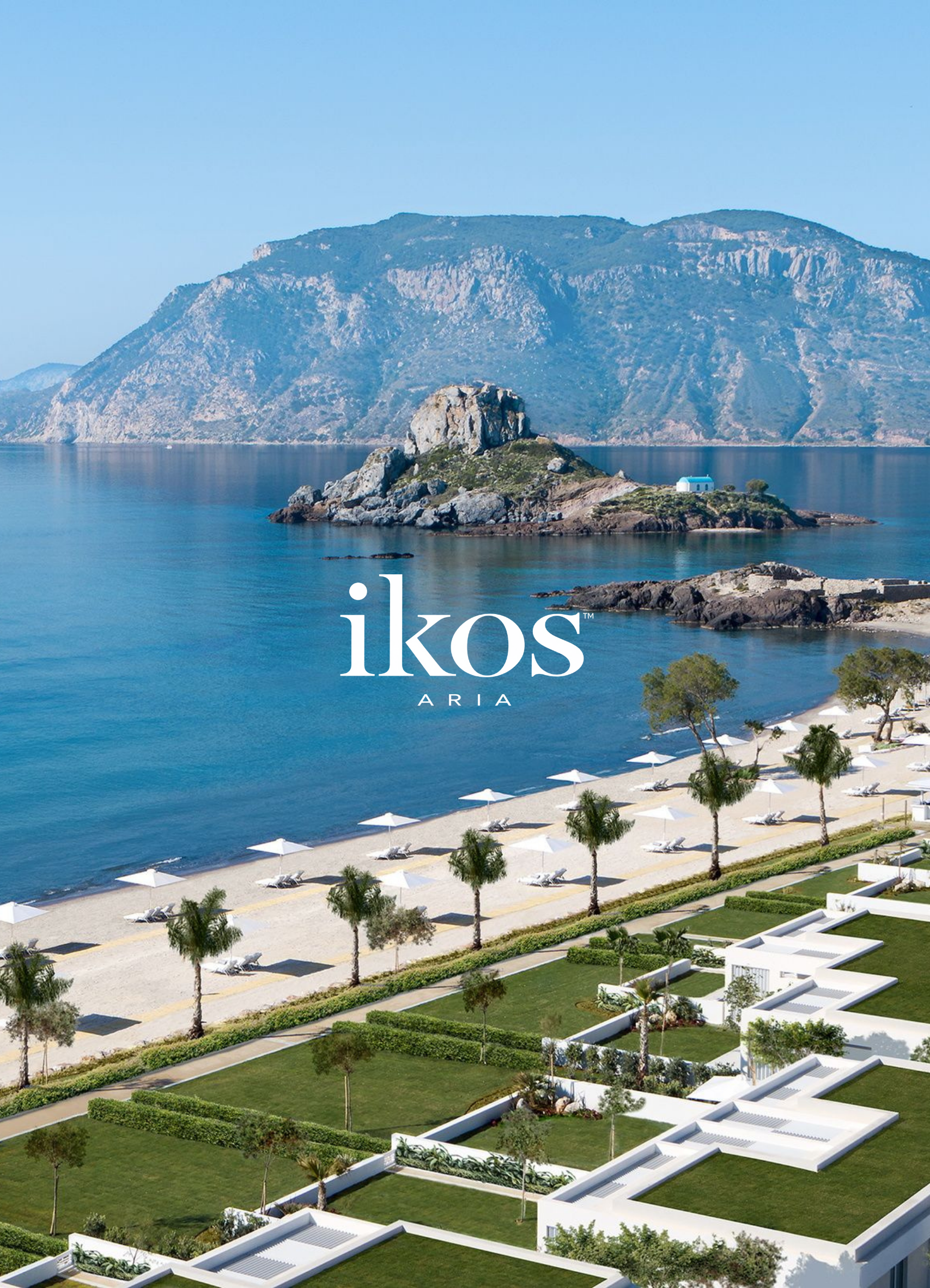 Scenic view of a large body of water with small island and rock formations, surrounded by mountainous terrain, with modern white buildings, trees, and lounge chairs along the beach area.
