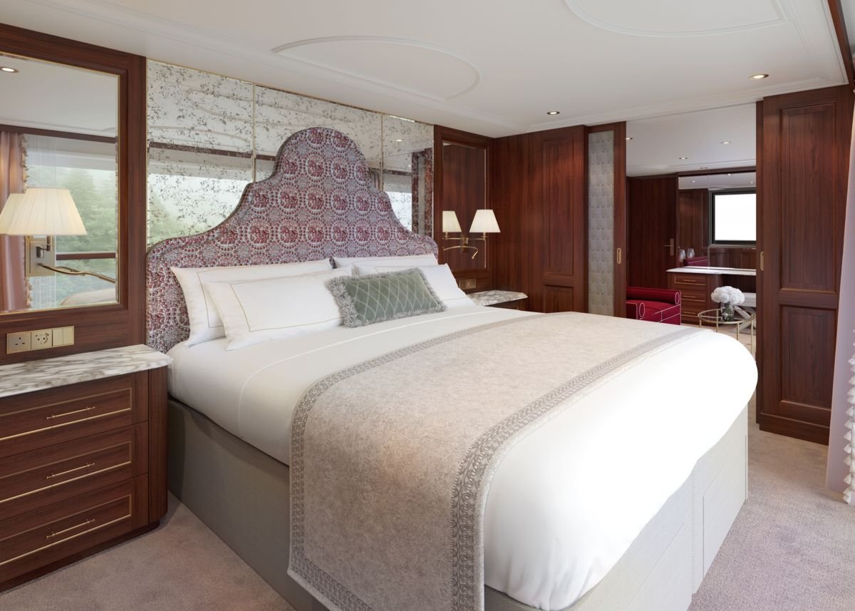 A luxurious bedroom with a large bed, decorative headboard, side tables, and wall-mounted lamps, featuring wood paneling and a window with a view of greenery.