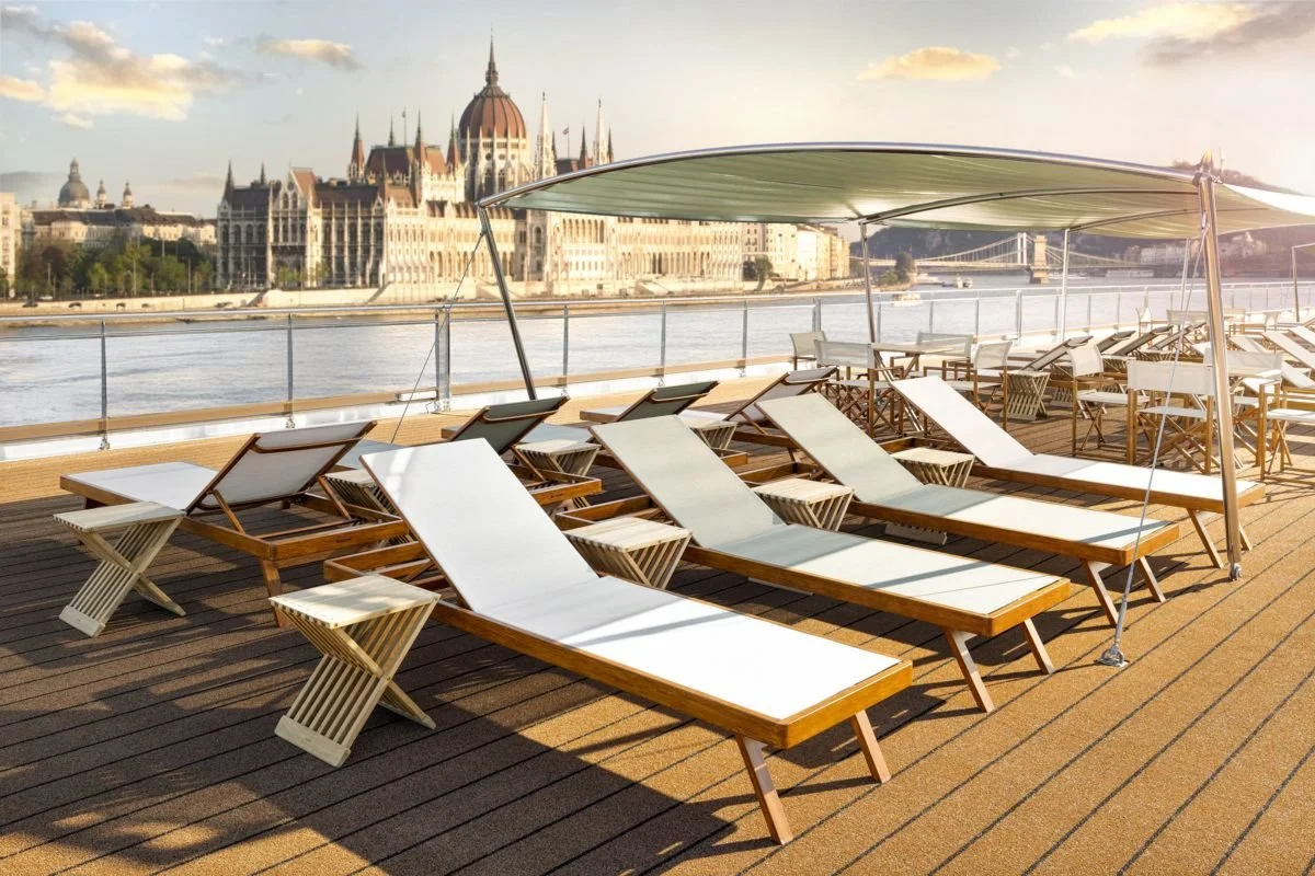 Sun loungers and small tables on a boat deck with the Hungarian Parliament Building across the river in Budapest, Hungary, during sunset.