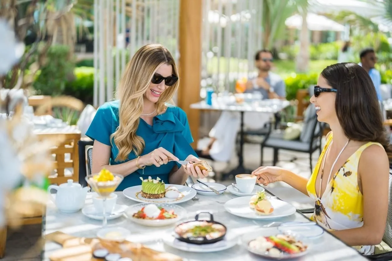 Women wearing sunglasses enjoying dessert and coffee at an outdoor restaurant table
