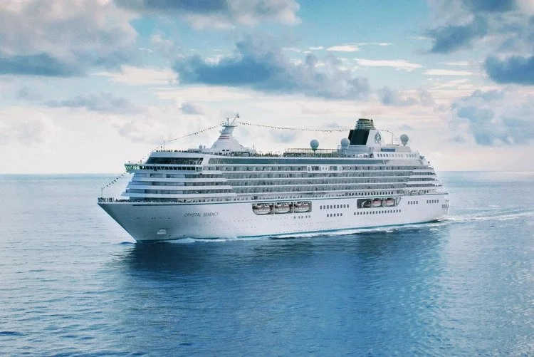 A large white cruise ship sailing on the ocean with a partly cloudy sky.