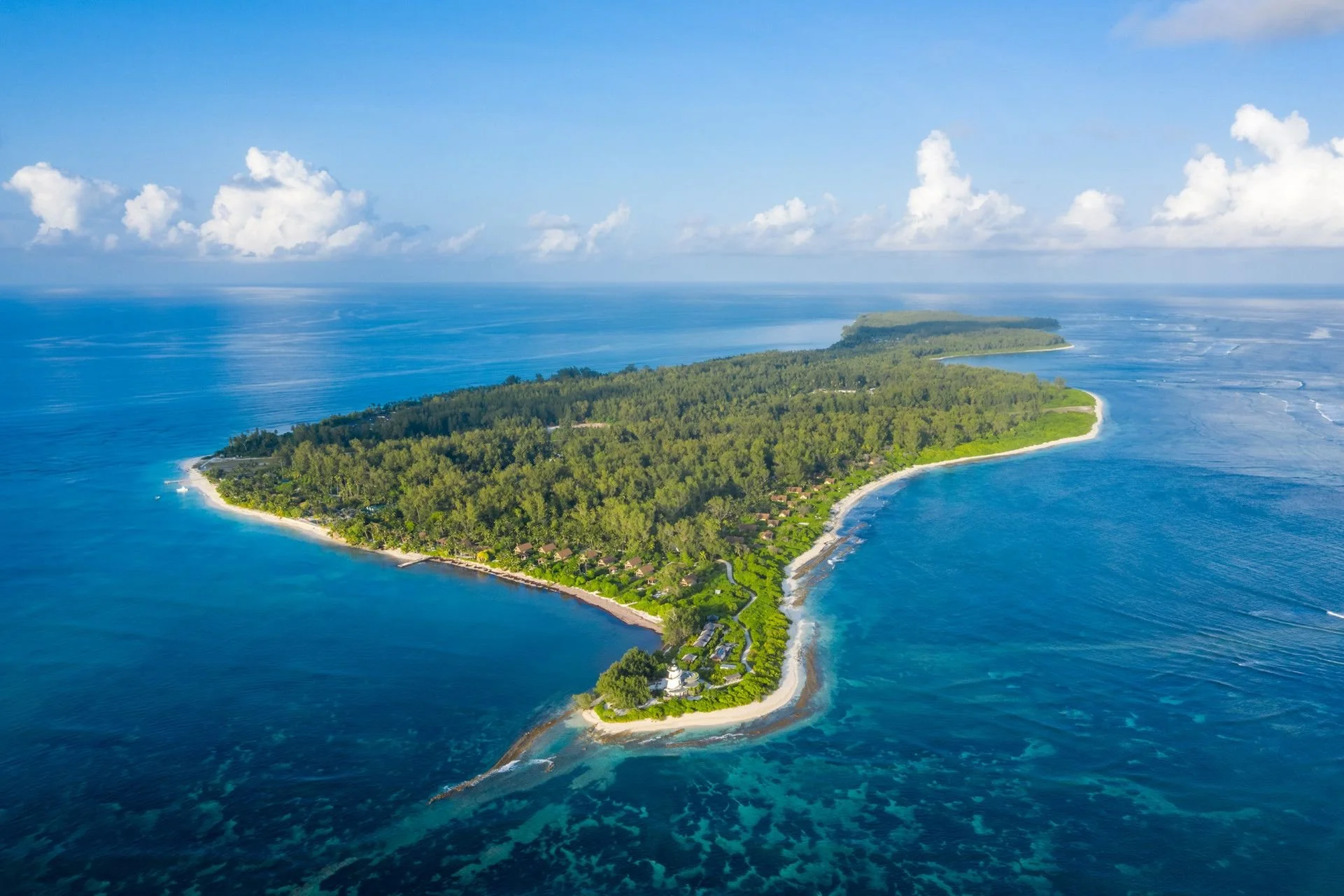 Aerial view of a lush, green island surrounded by blue ocean waters, with a small coastal settlement visible near the shoreline.