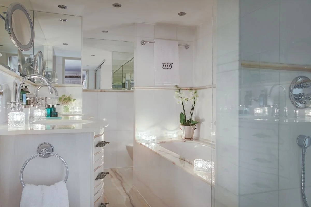 A luxurious bathroom with a bathtub, a mirror, and a vanity with toiletries, decorated with a potted orchid and illuminated by soft lighting.
