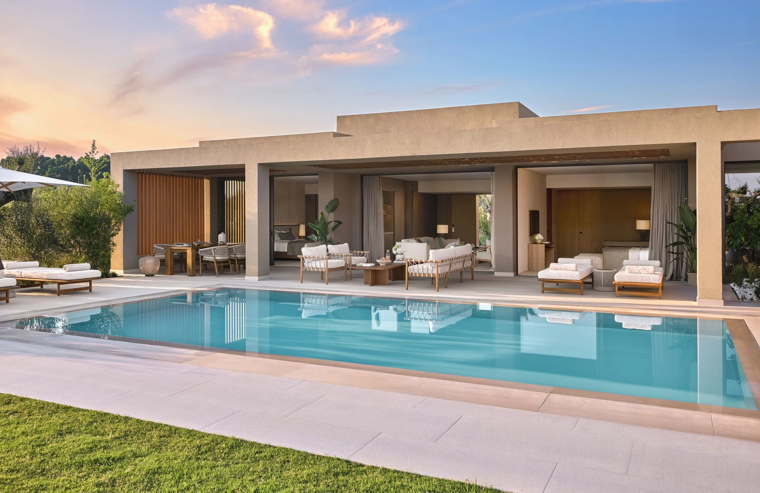 Modern house with indoor-outdoor living space, large swimming pool, and sunset sky.