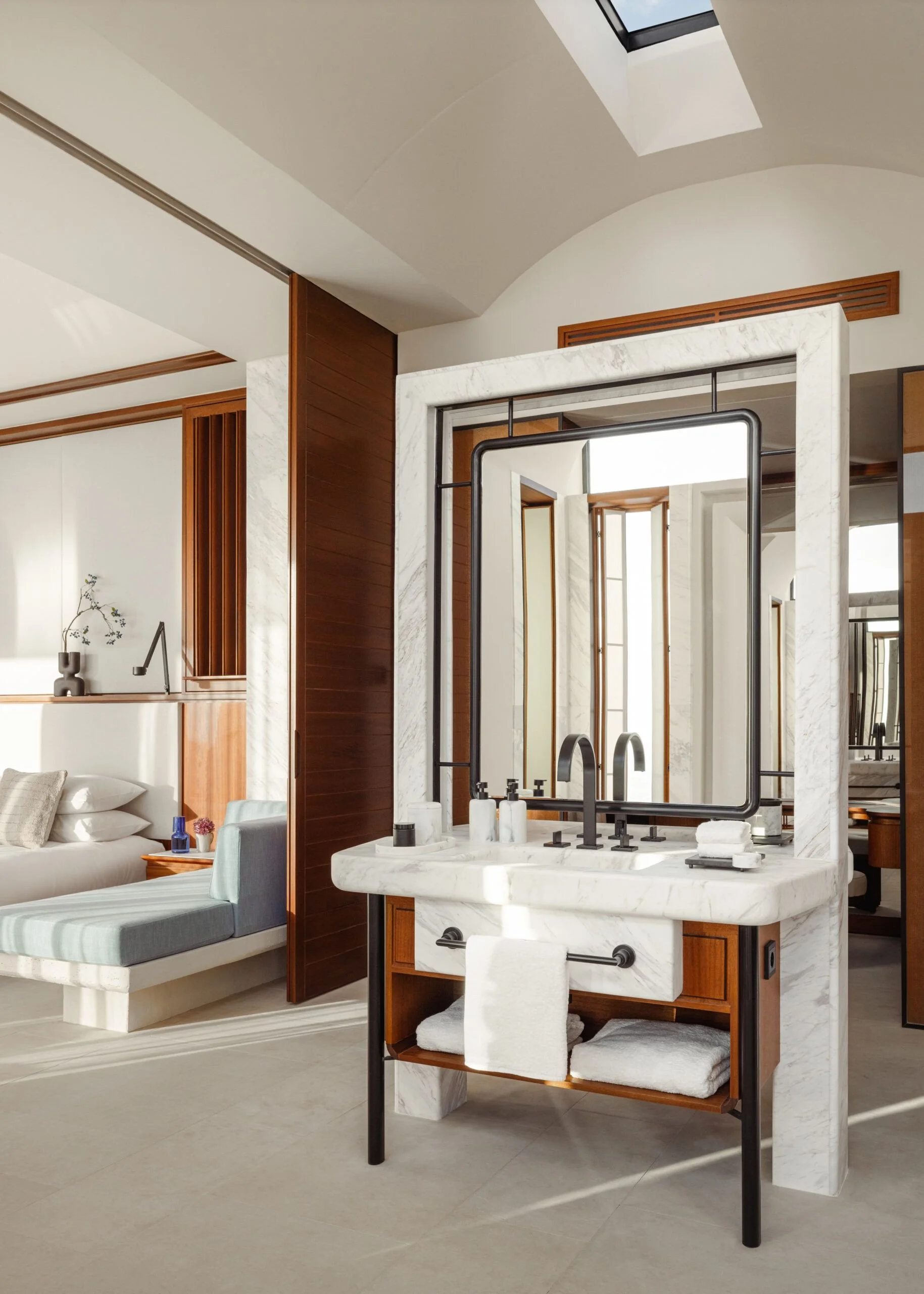 Modern bathroom vanity with a marble countertop, black fixtures, and a large mirror framed in black metal; part of a spacious and well-lit room with a view of an adjacent bedroom.