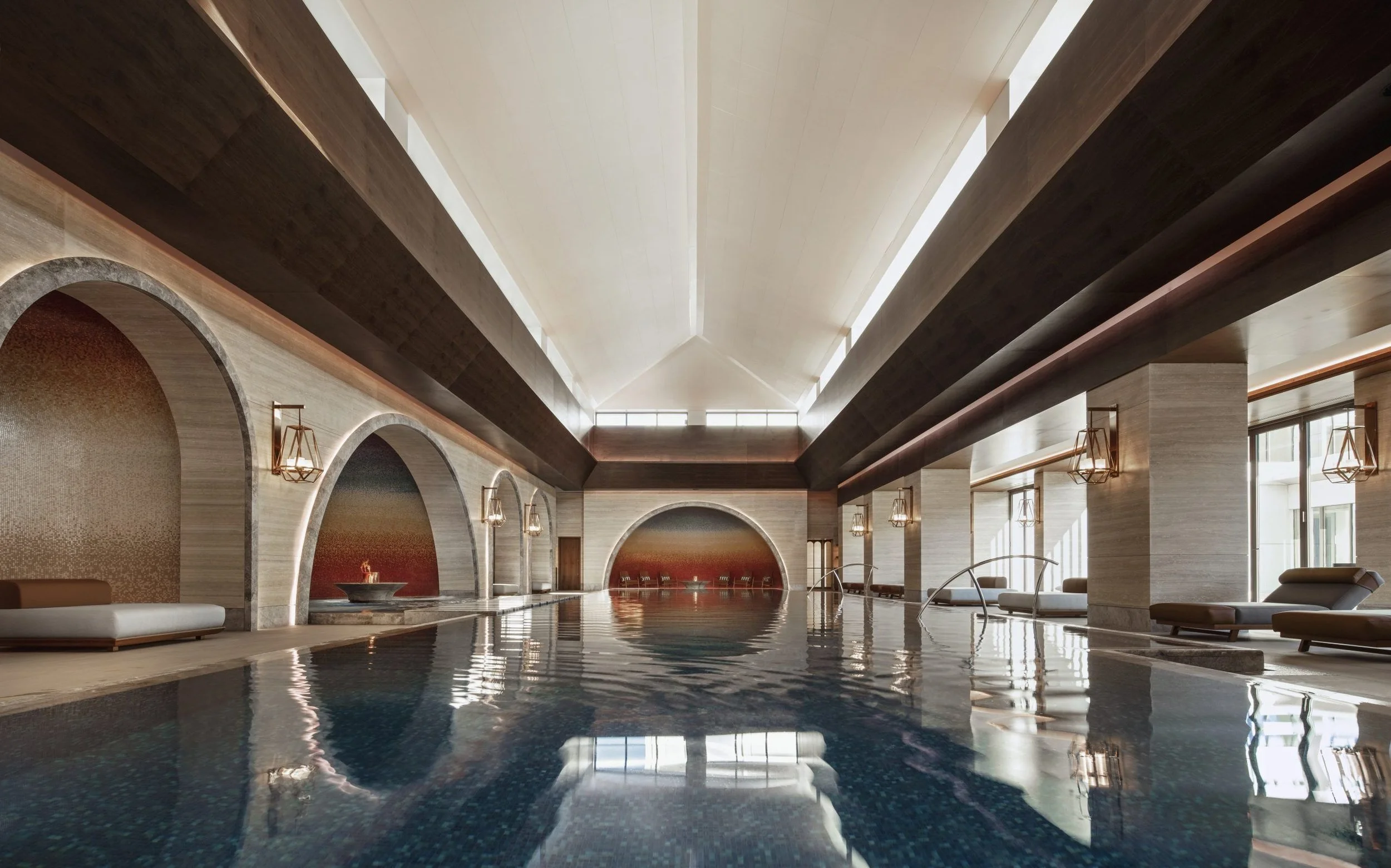 Luxury indoor swimming pool with high vaulted ceiling, large windows, modern lighting fixtures, and elegant architectural details.